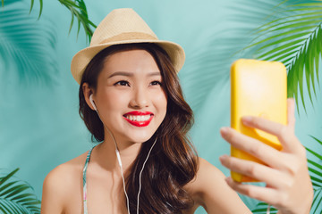 Pretty smiling asian woman using smartphone take selfie photo standing over blue background
