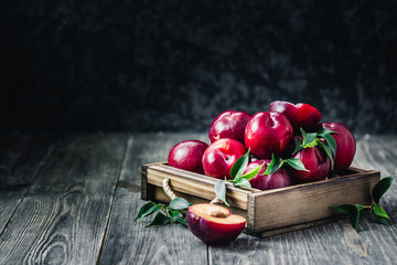 Fresh ripe plums in wooden box on rustic, wooden background. Selective focus, space for text.