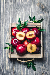 Fresh purple plums in wooden box on rustic wooden background. Top view, space for text.