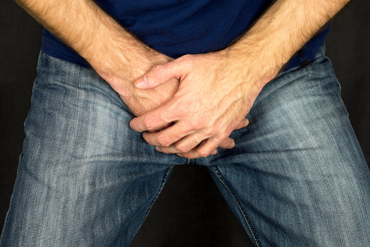  Erectile dysfunction concept. Close up of a man with hands holding his crotch dark background. Men's health. The pain from the blow in groin