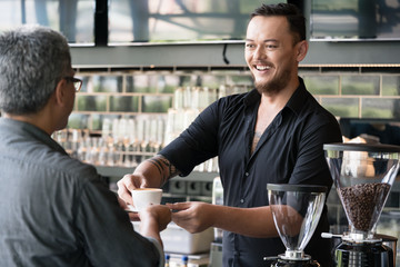 Friendly bartender serving espresso coffee to a middle-aged customer in the interior of a modern coffee shop