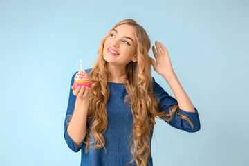 Happy young woman with birthday cupcake on color background