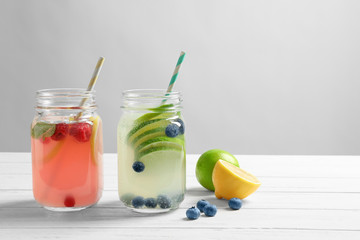Tasty lemonades with berries and lime in mason jars on table