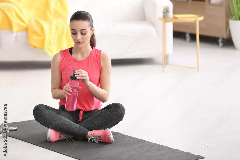 Sticker Beautiful young woman with bottle of water after doing fitness exercises at home