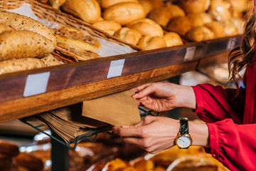 partial view of woman taking paper bag for bread while shopping in supermarket