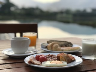 English breakfast with fried egg, bacon, toasts, coffee and orange juice on mountain background in sunshine day   