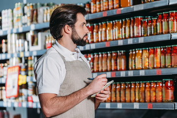 side view of shop assistant in apron with notebook in supermarket