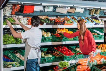 side view of shop assistant in apron and female shopper in hypermarket