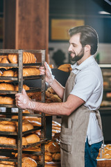 smiling male shop assistant arranging fresh pastry in supermarket
