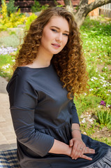 Obraz premium Lovely woman with chic curly hair resting in the backyard of his country house on a background of a blossoming lawn.