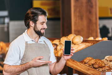 portrait of smiling shop assistant showing smartphone with blank screen in supermarket