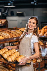 smiling shop assistant arranging loafs of bread in shopping market
