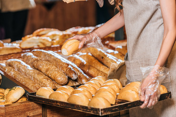 partial view of shop assistant arranging loafs of bread in shopping market
