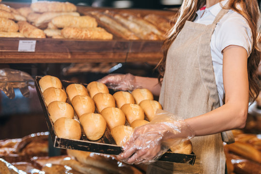 partial view of shop assistant arranging loafs of bread in shopping market