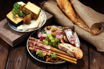 Italian antipasti wine snacks set. Cheese variety, Mediterranean olives, pickles, Prosciutto di Parma, salami and wine in glasses over black grunge background.