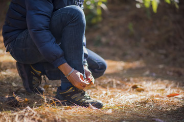 Young hiker man ties the laces on his shoe during a holiday backpacking in forest.