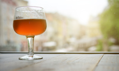A glass of beer on a wooden table by the window. Free space