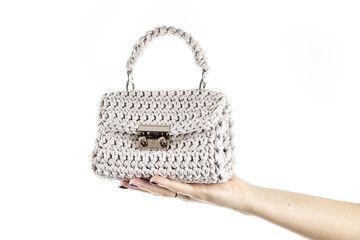 Woman's hand is holding a small crocheted cross body bag of beige color isolated on white background. - 198187775
