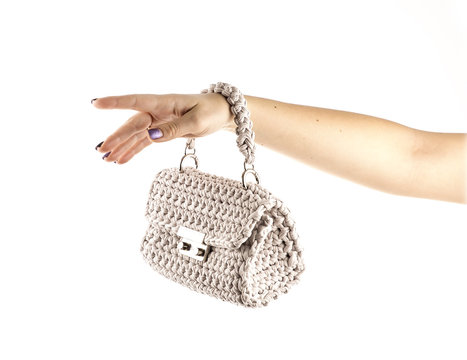 Woman's hand is holding a small crocheted cross body bag of beige color isolated on white background.