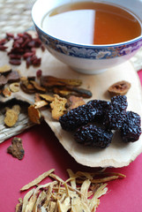 Goji berries, chinese dates, astragalus root pieces with a bowl of herb tea on red background....