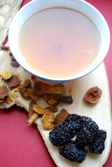 Goji berries, chinese dates, astragalus root pieces with a bowl of herb tea on red background. Vertical photo.