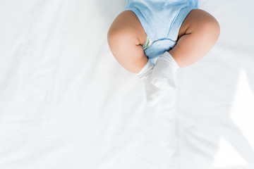 cropped shot of little child in rompers and white socks lying on bed