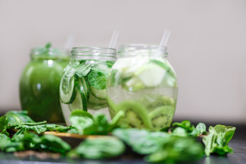 Blended green smoothie and infused detox water with cucumber, mint, kiwi spinach and apple for diet healthy eating and weight loss with space for a text. Grey backfround