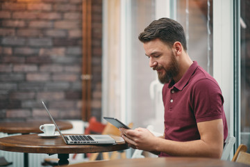 Young man sitting in cafeteria and using tablet computer