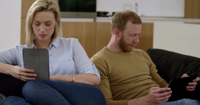 Attractive couple surf on tablets whist ignoring each other, showing what is wrong with modern technology