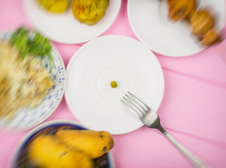 The concept of starvation, bulimia. A pea on a fork surrounded by blurry dishes.