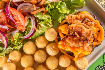 Delicioso hamburguer com cheddar e bacon, acompanhado de batata e salada.