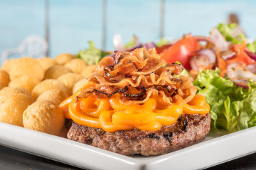 Delicioso hamburguer com cheddar e bacon, acompanhado de batata e salada.