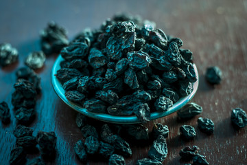 Black raisin or kali kishmish or Zante currant in a white plate on wooden surface in dark Gothic...