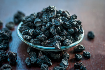 Black raisin or kali kishmish or Zante currant in a white plate on wooden surface in dark Gothic...
