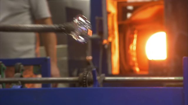 A steady medium shot from inside a glass factory where a man works on a glass.