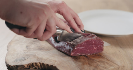 female hands slicing raw beef fillet for steak on wooden board