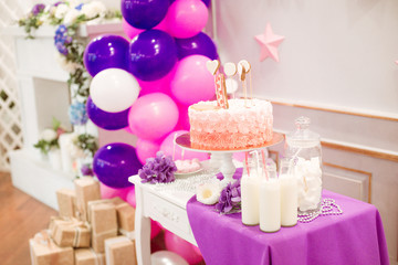 A lovely delicious candy bar in pink and purple colors for a little princess on her 1st birthday. Beautifully decorated children's party with balloons flowers and sweets