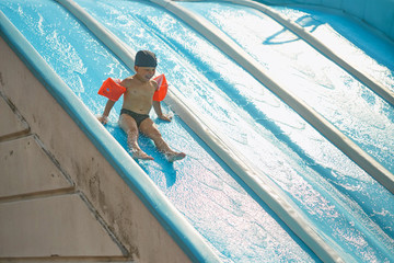 child in armlets for swimming in an outdoor pool with a water slide.