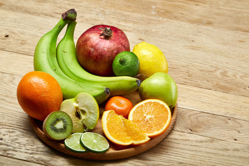 Ripe fresh fruits in a wooden plate on a light wooden background, selective focus, close-up, top view