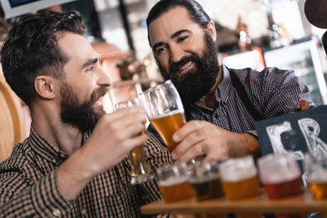 Happy bearded men try beer of different styles in beer samplers in brewery of craft beer.
