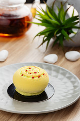 Mini mousse cake covered with yellow chocolate velour on gray plate