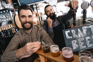 Happy bearded men test beer of different styles in beer samplers in brewery of craft beer.