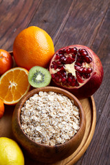 Bowl with oatmeal flakes served with fruits on wooden tray over rustic background, flat lay, selective focus
