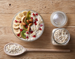 Composition with bowl of oatmeal porrige and dry oatmeal in glassware on wooden table indoors