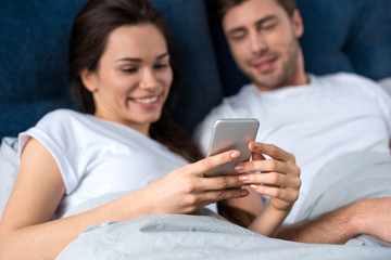 Woman using smartphone while lying in bed with her husband