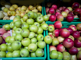 On the shop window in the boxes are red and green apples and pears.
