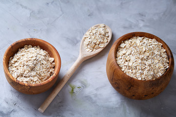 Two bowls with oat flakes and wooden spoon isolated on white background, close-up, top view, selective focus.