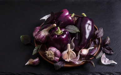 Fresh vegetable violet pepper with leaves of basil with garlic in the rustic plate on black stone  table. top view.