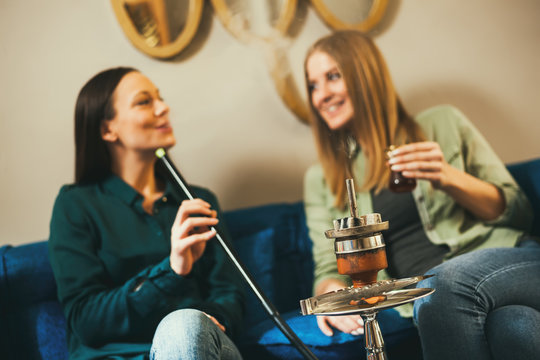 Two happy women are sitting in shisha bar and smoking nargile 