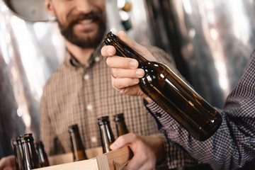 Brewer holds empty beer bottle in hand. Stages of brewing production. Process of beer manufacturing.